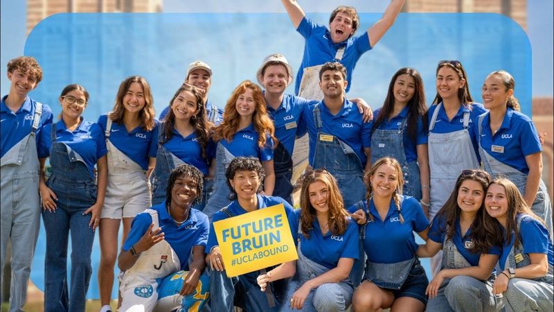 A group of transfer students admitted to UCLA wearing matching blue UCLA shirts and overalls pose together for a photo with a "FUTURE BRUIN #UCLABOUND" sign in the center
