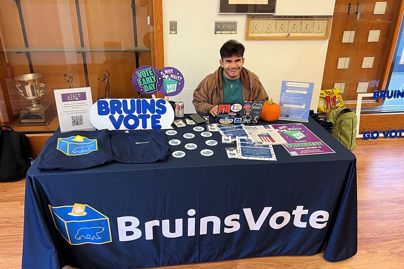 A smiling student sits at a Bruins Vote table ready to help students register to vote.