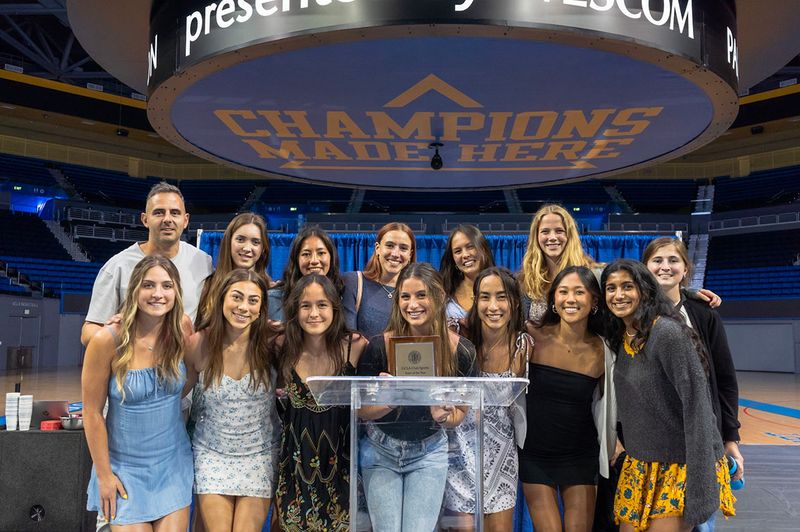 Club sports members pose in Pauley Pavilion holding a "team of the year" award
