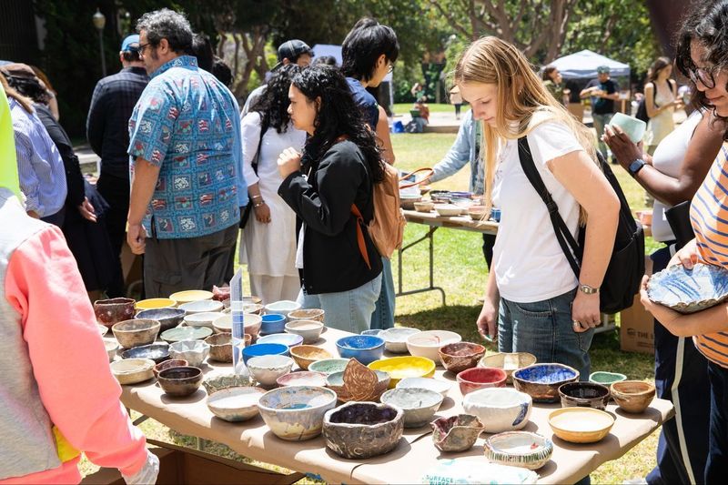 People look at dozens of ceramic bowls displayed on a table outdoors